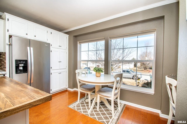 dining area featuring light wood-style floors, crown molding, and baseboards