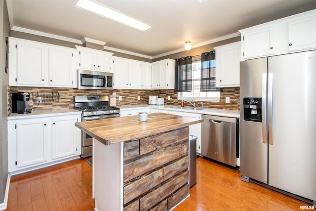 kitchen with white cabinets, appliances with stainless steel finishes, ornamental molding, light wood-style floors, and a sink