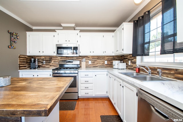 kitchen featuring tasteful backsplash, ornamental molding, stainless steel appliances, light wood-style floors, and a sink