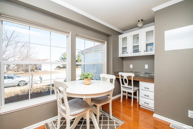 dining area with a healthy amount of sunlight, light wood-style flooring, ornamental molding, and built in desk