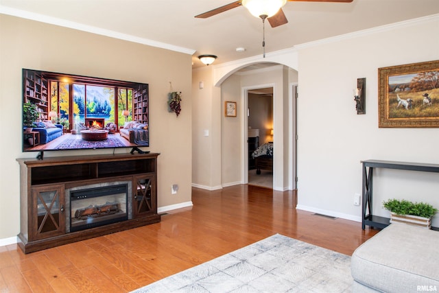 living room with ornamental molding, arched walkways, baseboards, and wood finished floors