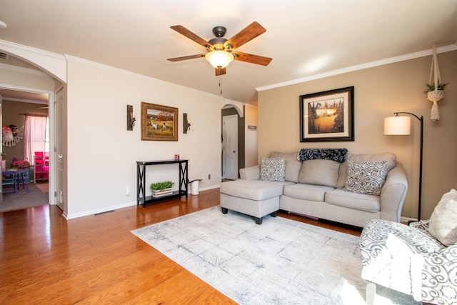 living area featuring arched walkways, wood finished floors, visible vents, baseboards, and crown molding