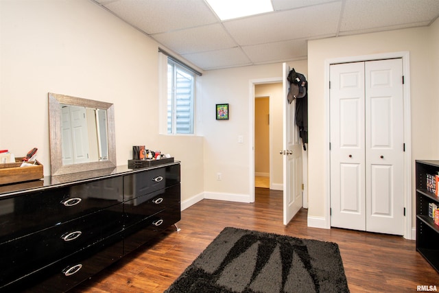 bedroom with dark wood-style floors, a paneled ceiling, a closet, and baseboards