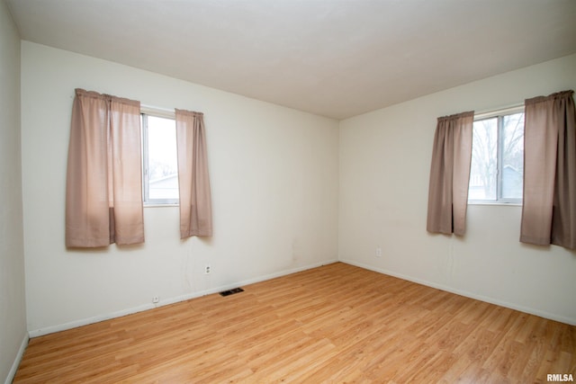 spare room featuring light wood-type flooring, visible vents, and baseboards