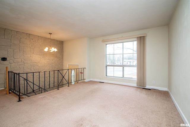 carpeted empty room featuring a chandelier, visible vents, and baseboards