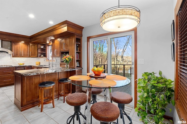 kitchen with tasteful backsplash, open shelves, dark stone counters, brown cabinets, and a sink