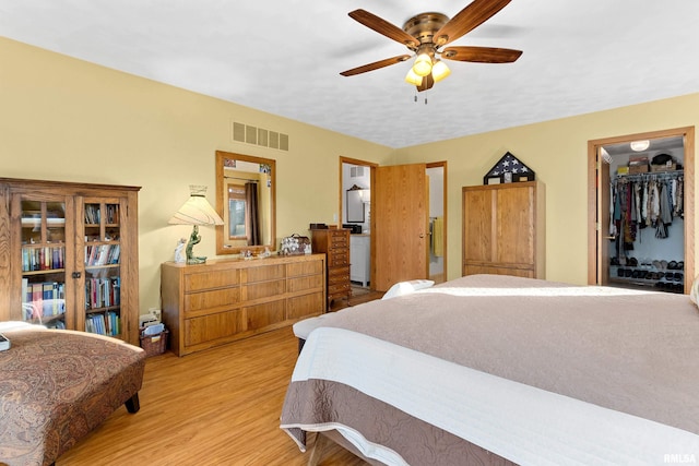 bedroom with wood finished floors, visible vents, a ceiling fan, a closet, and a walk in closet