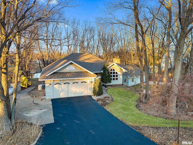 view of front of house with a front lawn, driveway, roof with shingles, a garage, and a chimney