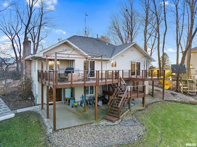 back of property featuring a deck, a patio area, a lawn, and roof with shingles