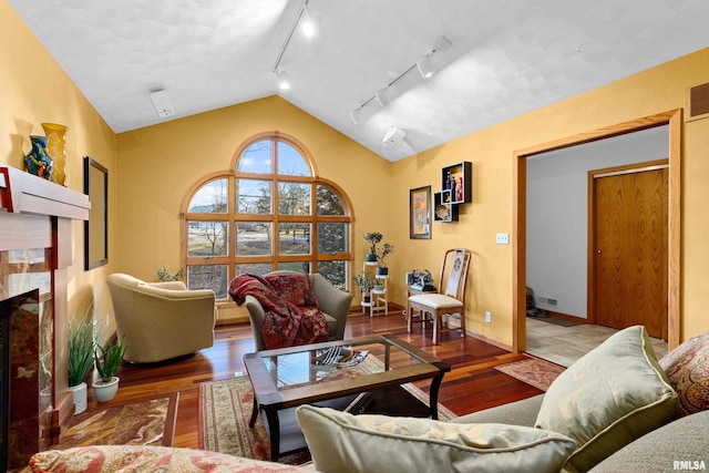 living area featuring wood finished floors, visible vents, baseboards, a fireplace, and vaulted ceiling