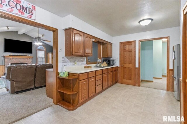 kitchen featuring vaulted ceiling with beams, light carpet, light countertops, freestanding refrigerator, and brown cabinets