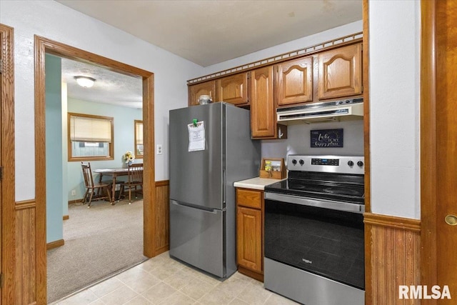 kitchen with under cabinet range hood, light carpet, light countertops, appliances with stainless steel finishes, and brown cabinets