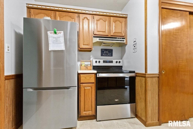 kitchen with under cabinet range hood, appliances with stainless steel finishes, light countertops, and wainscoting