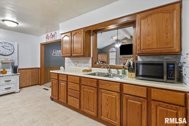 kitchen with brown cabinetry, wainscoting, stainless steel microwave, light countertops, and a sink