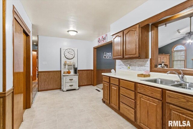 kitchen with brown cabinets, a wainscoted wall, light countertops, a ceiling fan, and a sink