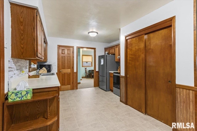 kitchen featuring stainless steel appliances, a sink, light countertops, light floors, and brown cabinetry