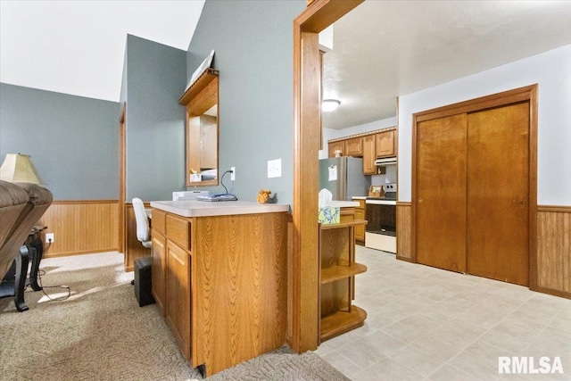 kitchen featuring light countertops, wainscoting, wood walls, and stove