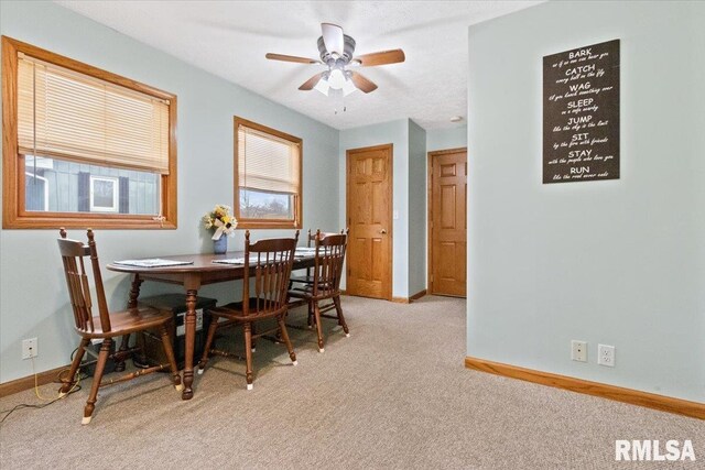 dining area with a ceiling fan, light colored carpet, and baseboards