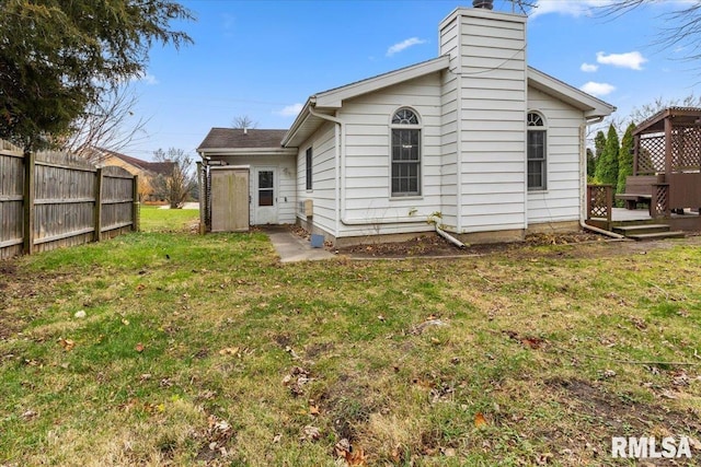 rear view of house featuring a chimney, fence, a deck, and a yard