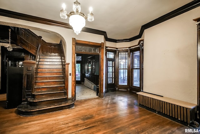 entrance foyer with radiator, wood finished floors, stairs, crown molding, and a notable chandelier