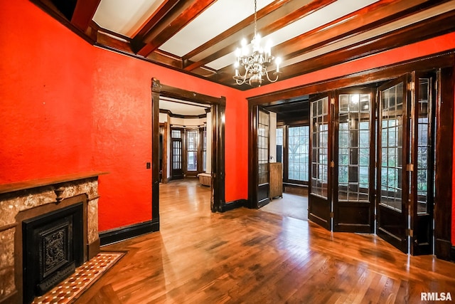 interior space with beamed ceiling, wood finished floors, an inviting chandelier, a fireplace, and baseboards