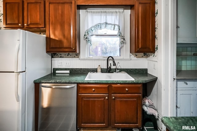 kitchen featuring dark countertops, backsplash, dishwasher, freestanding refrigerator, and a sink