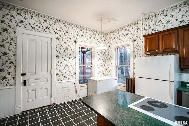 kitchen featuring wallpapered walls, cooktop, wainscoting, and freestanding refrigerator