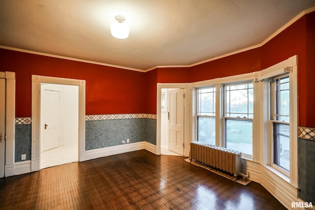 empty room with hardwood / wood-style floors, radiator heating unit, baseboards, and ornamental molding