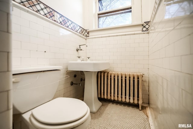 half bathroom with tile walls, a wainscoted wall, toilet, and radiator heating unit