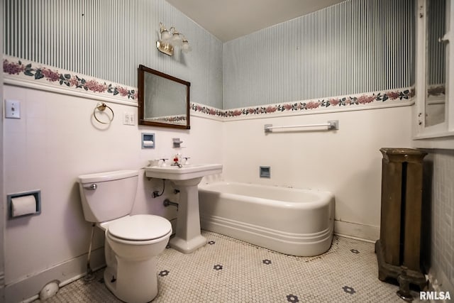 bathroom with tile patterned flooring, baseboards, toilet, a tub to relax in, and a sink