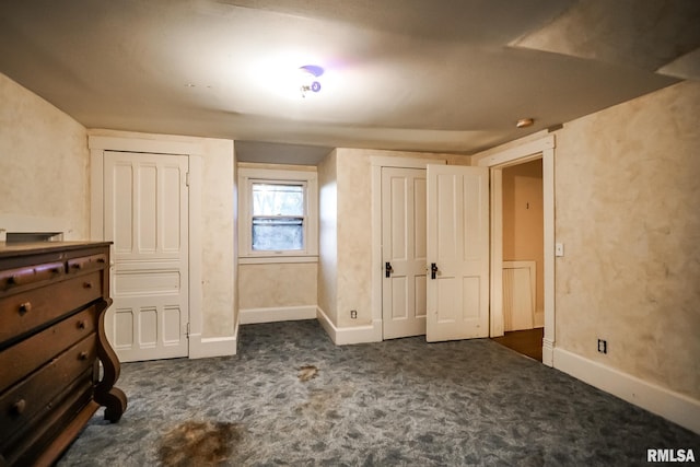 unfurnished bedroom featuring baseboards, multiple closets, and dark colored carpet