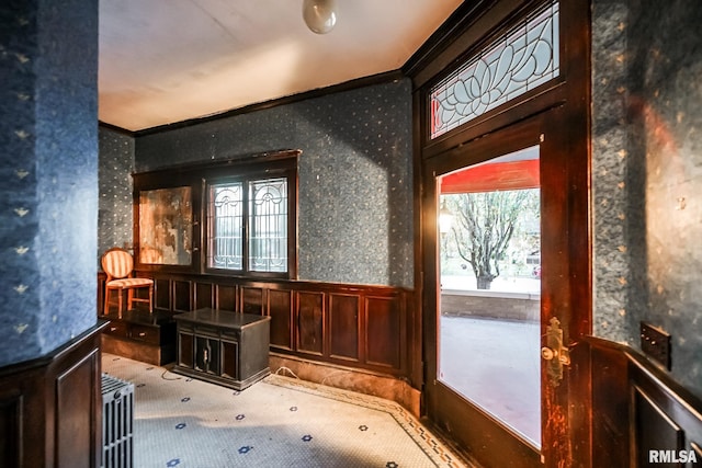 doorway to outside with crown molding, wainscoting, and wallpapered walls