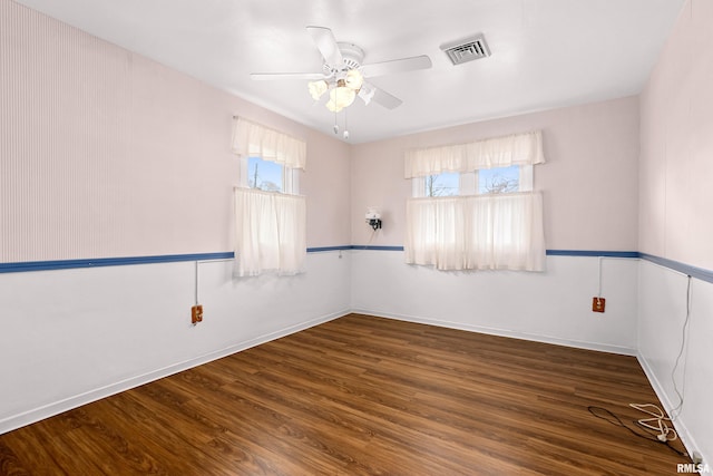 empty room featuring a ceiling fan, wood finished floors, visible vents, and a wealth of natural light