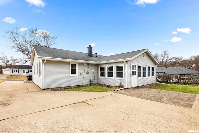 back of property with a shingled roof, concrete driveway, and a chimney