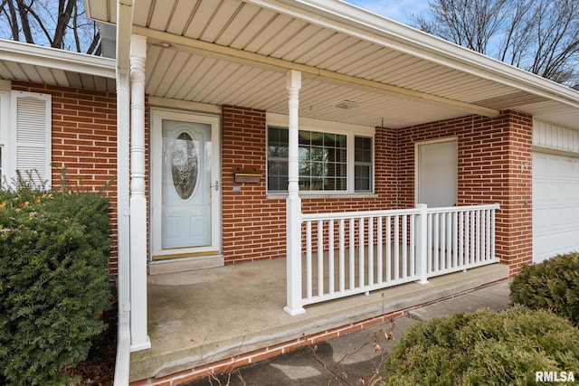 view of exterior entry featuring a porch, an attached garage, and brick siding