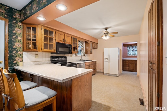 kitchen featuring wallpapered walls, light countertops, brown cabinets, black appliances, and a sink