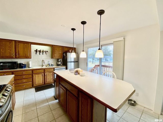 kitchen featuring brown cabinets, backsplash, stainless steel appliances, light countertops, and hanging light fixtures