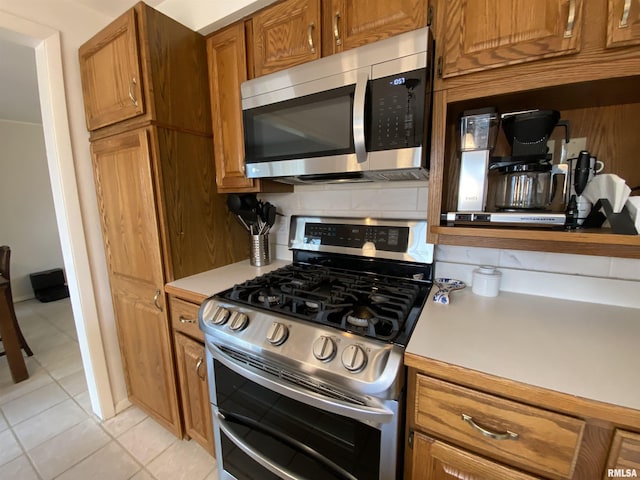 kitchen with tasteful backsplash, stainless steel appliances, brown cabinetry, light countertops, and light tile patterned floors