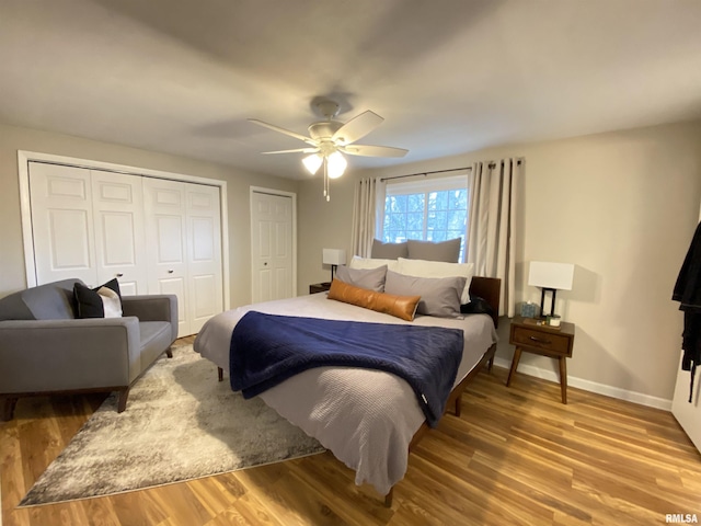 bedroom with baseboards, two closets, wood finished floors, and a ceiling fan