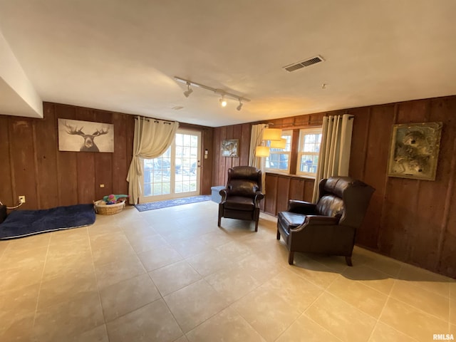 living area with track lighting, visible vents, and wood walls