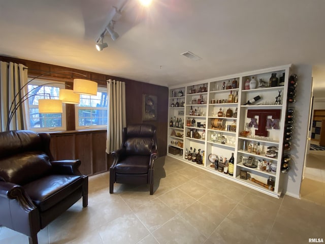 sitting room featuring tile patterned floors, visible vents, and wooden walls