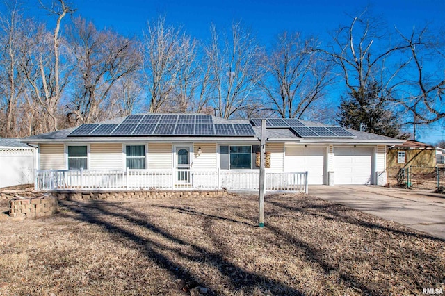 ranch-style home with roof mounted solar panels, an attached garage, concrete driveway, and fence