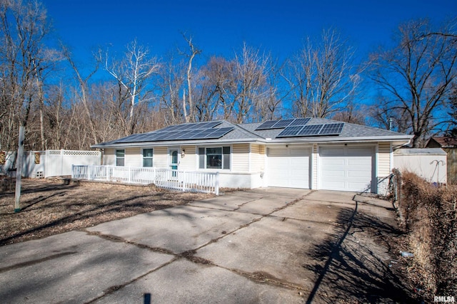 ranch-style home featuring fence, solar panels, an attached garage, a shingled roof, and concrete driveway