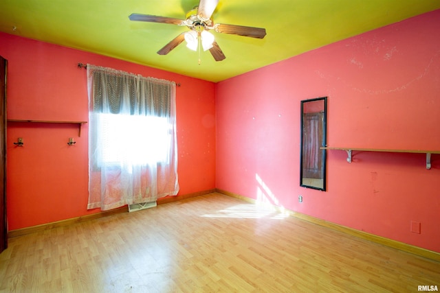 empty room featuring a ceiling fan, wood finished floors, visible vents, and baseboards