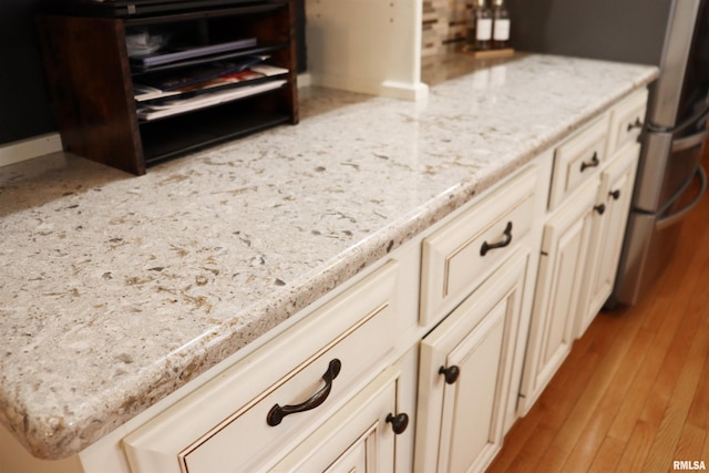 details featuring wood finished floors, cream cabinets, and light stone countertops