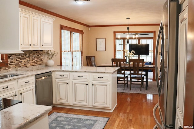 kitchen featuring a peninsula, light wood-style flooring, stainless steel appliances, decorative backsplash, and crown molding