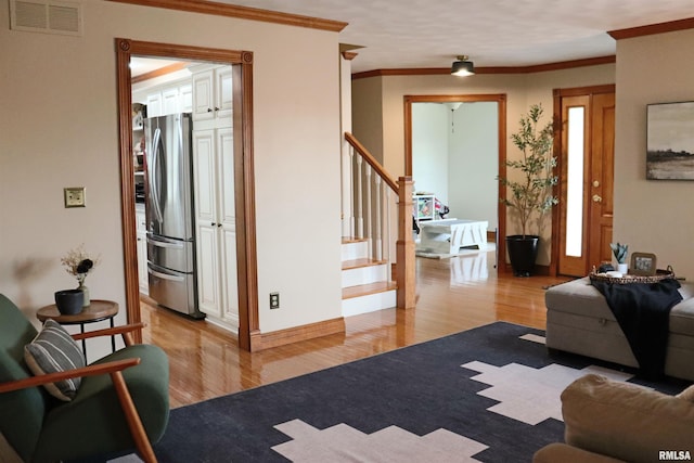 living room with visible vents, stairs, light wood-style floors, and ornamental molding