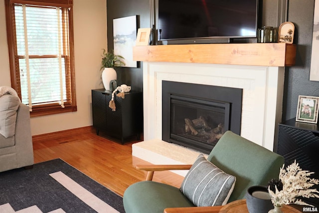 living area with baseboards, wood finished floors, and a glass covered fireplace