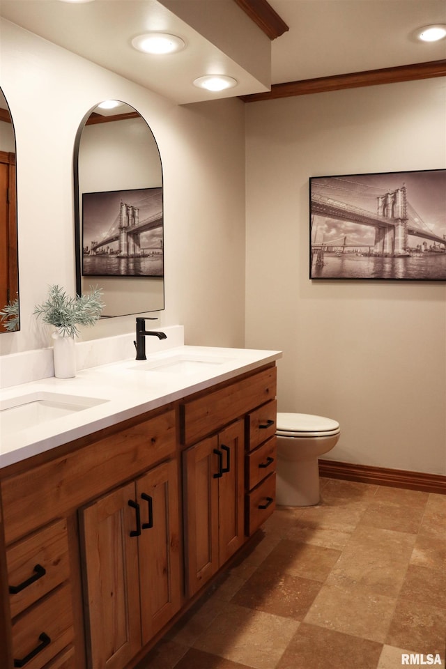 bathroom with a sink, baseboards, toilet, and double vanity