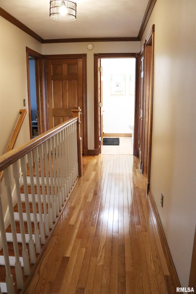 hallway with an upstairs landing, light wood-type flooring, baseboards, and ornamental molding